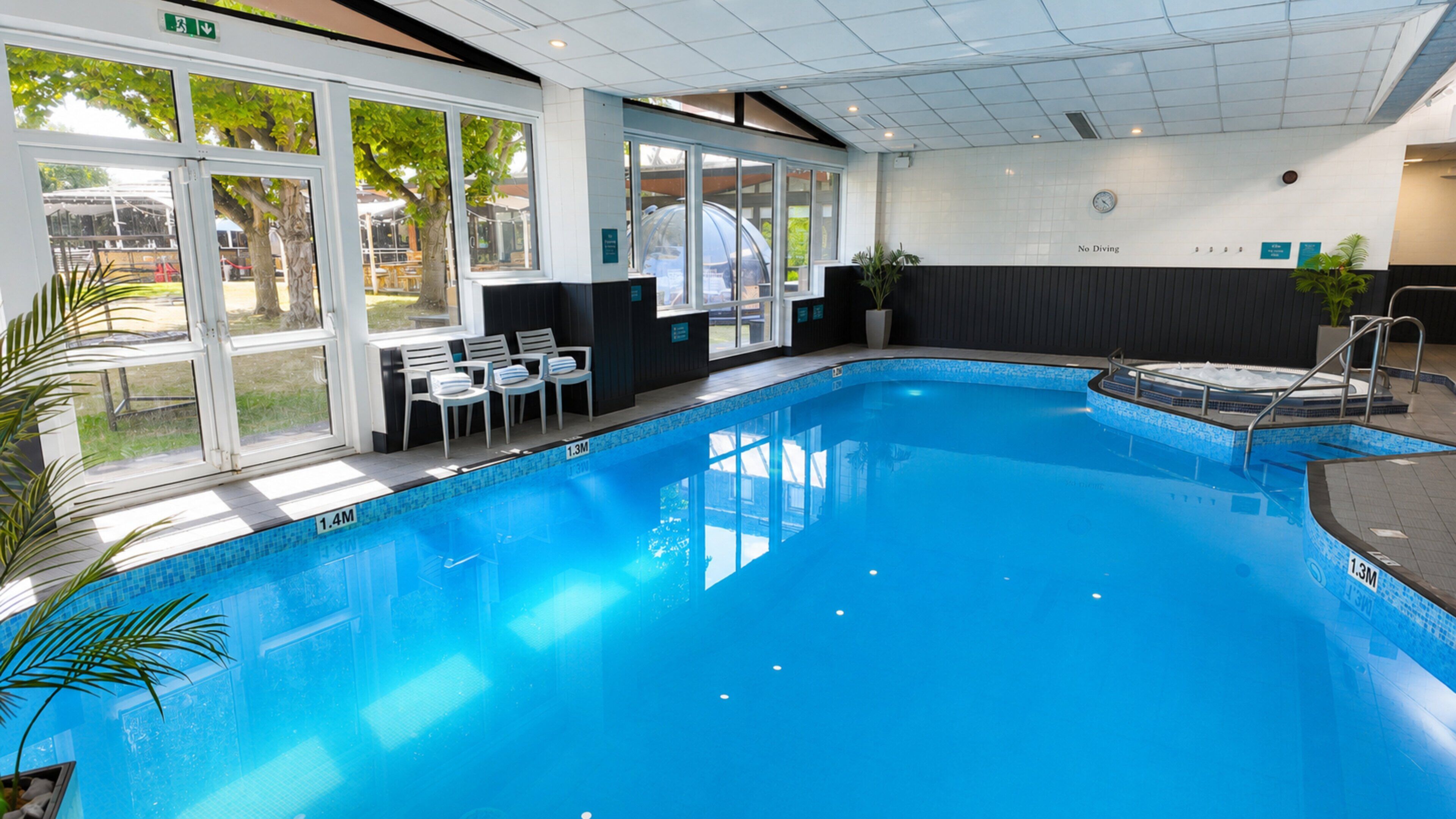 Une piscine intérieure à l’eau claire, dotée d’un plongeoir et d’un espace détente avec des chaises et des tables.