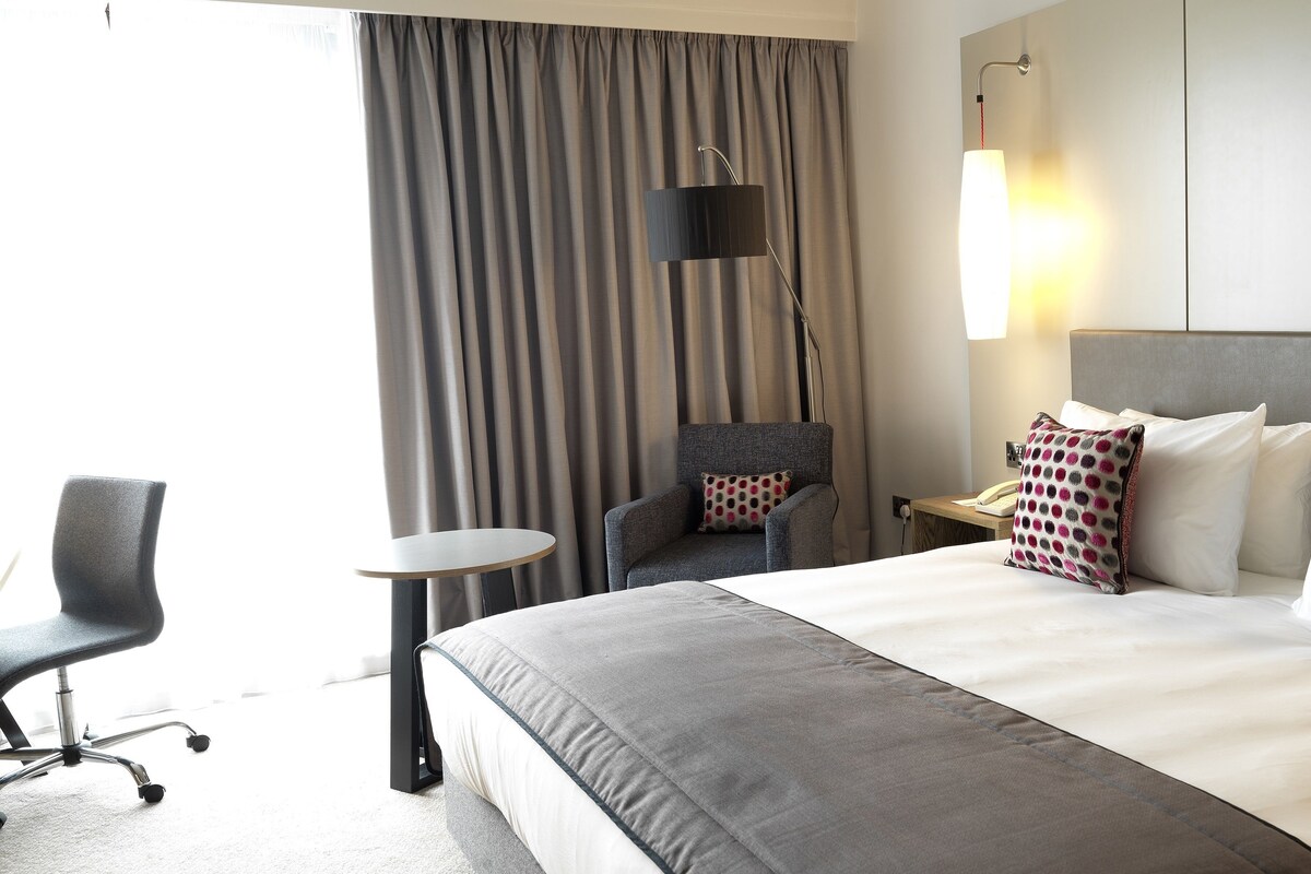 Una habitación de hotel con una cama grande, una silla, una mesita y una lámpara.