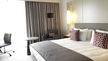 A hotel room with a large bed, a chair, a small table, and a lamp.