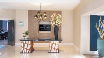 A reception desk with a sign for Crowne Plaza, a chandelier, a vase with flowers, and a potted plant.