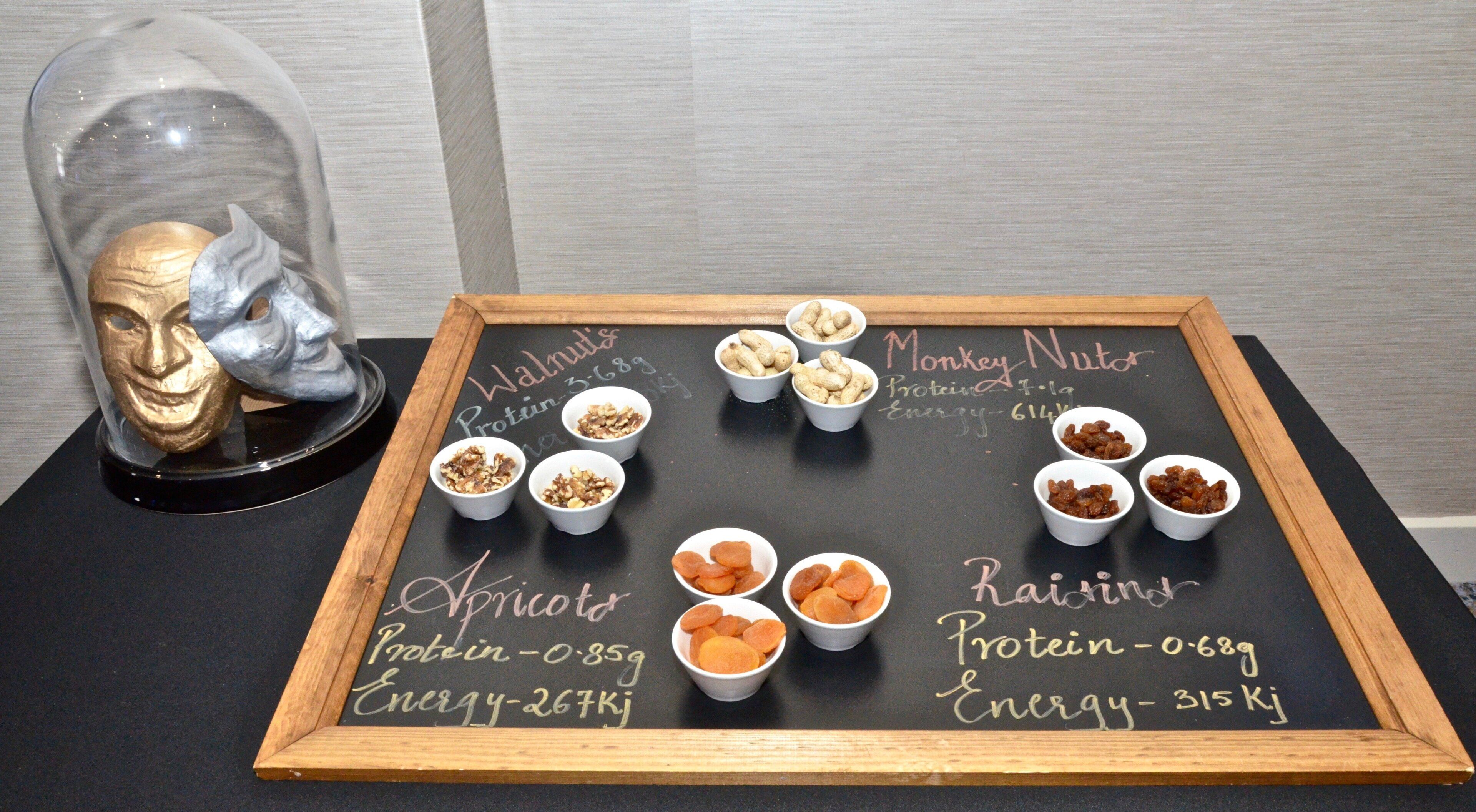 A chalkboard with nutritional information for apricots, raisins, and monkey nuts, along with small bowls containing these items.
