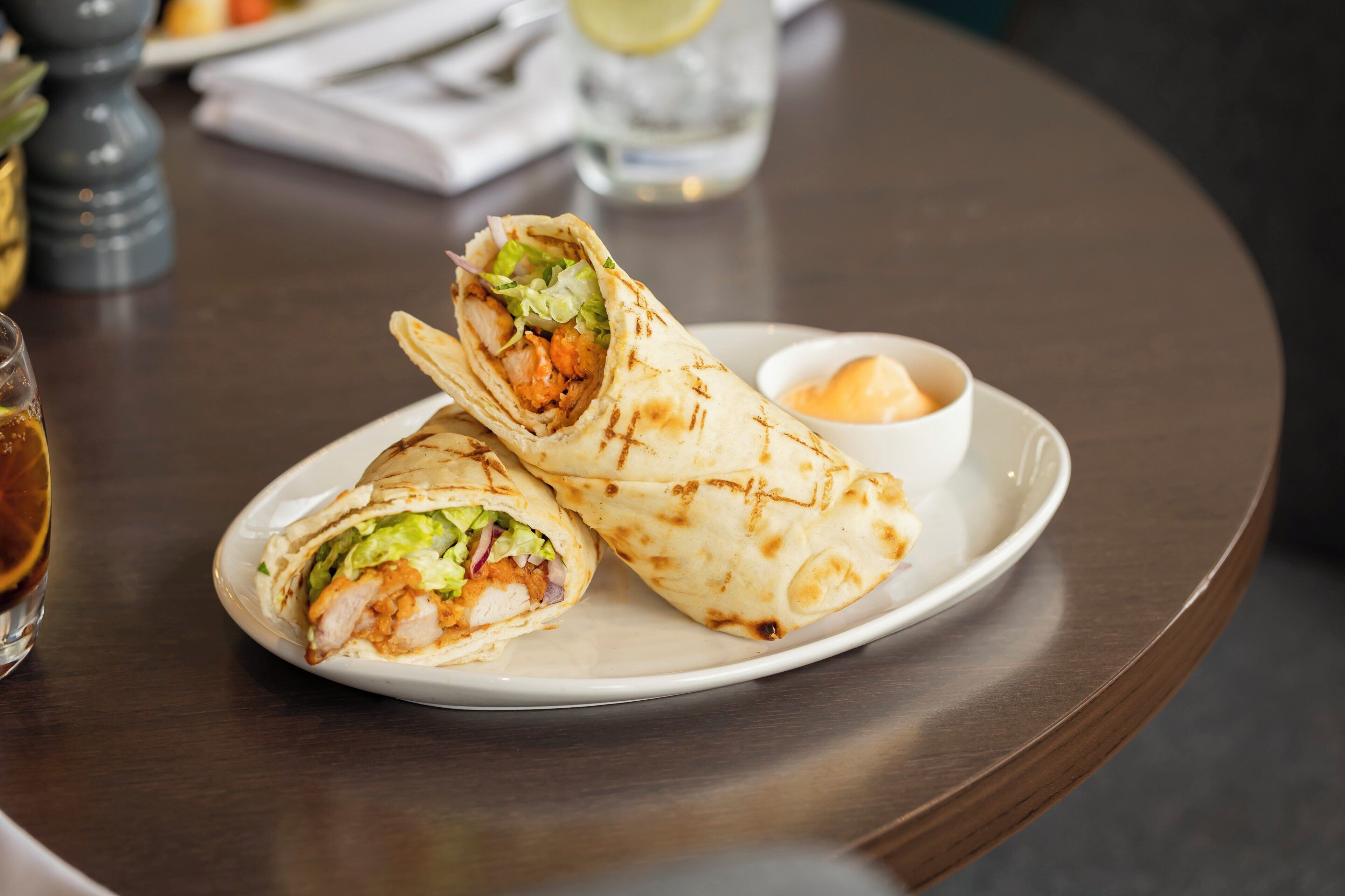 A plate with a wrap and a small bowl of sauce on a round table.