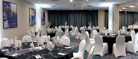 A banquet hall with round tables, white chairs, and black tablecloths.