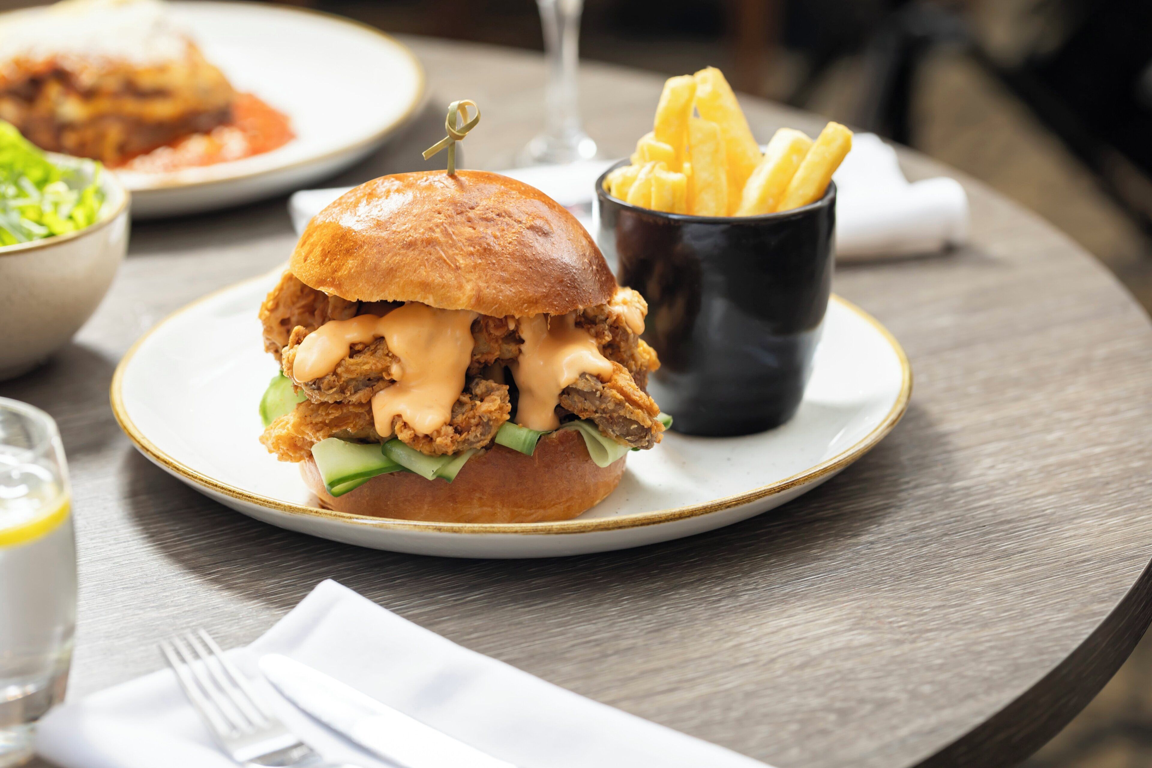 A sandwich with fries on a plate, a glass of water, and a fork on a table.