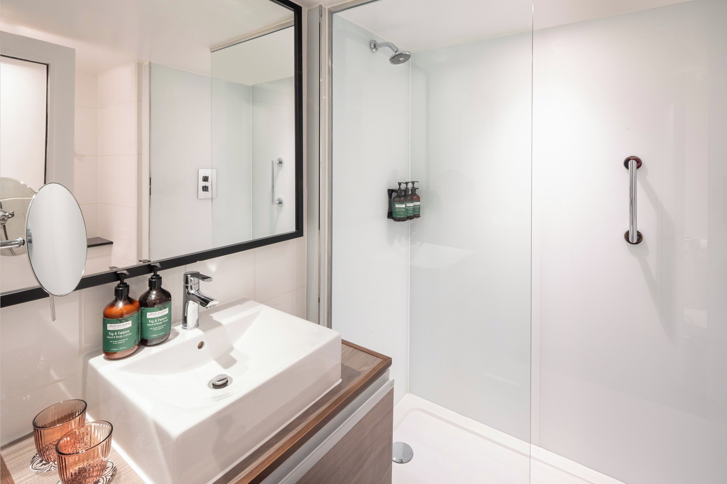 Un baño moderno con un espejo grande, un lavabo blanco y una ducha con cerramiento de vidrio.
