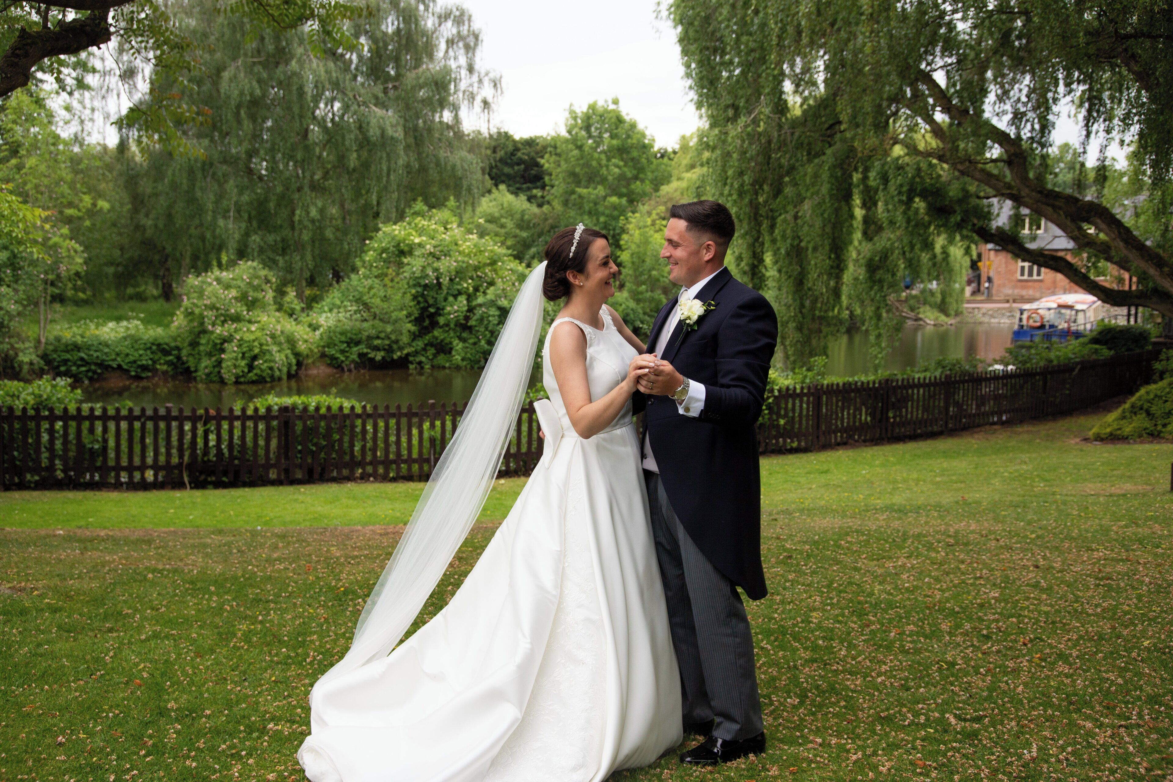 A couple embracing in a lush garden setting with a wooden fence and greenery in the background.