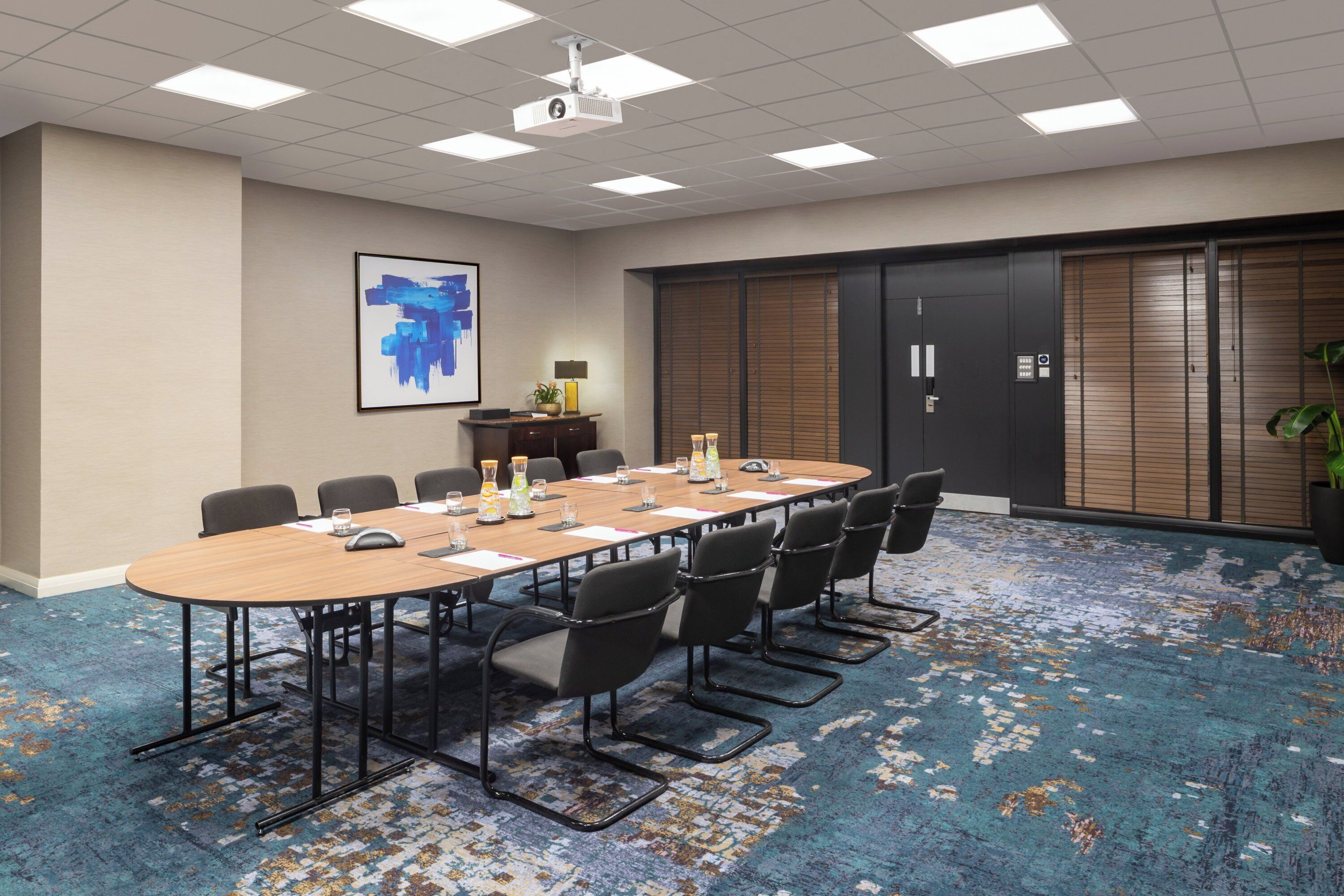 A conference room with a long table, chairs, a projector, and a large abstract painting on the wall.