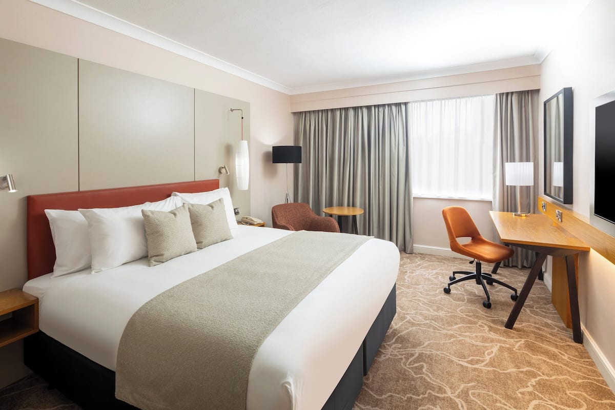A hotel room with a large bed, a desk, a chair, a TV, and a window with curtains.