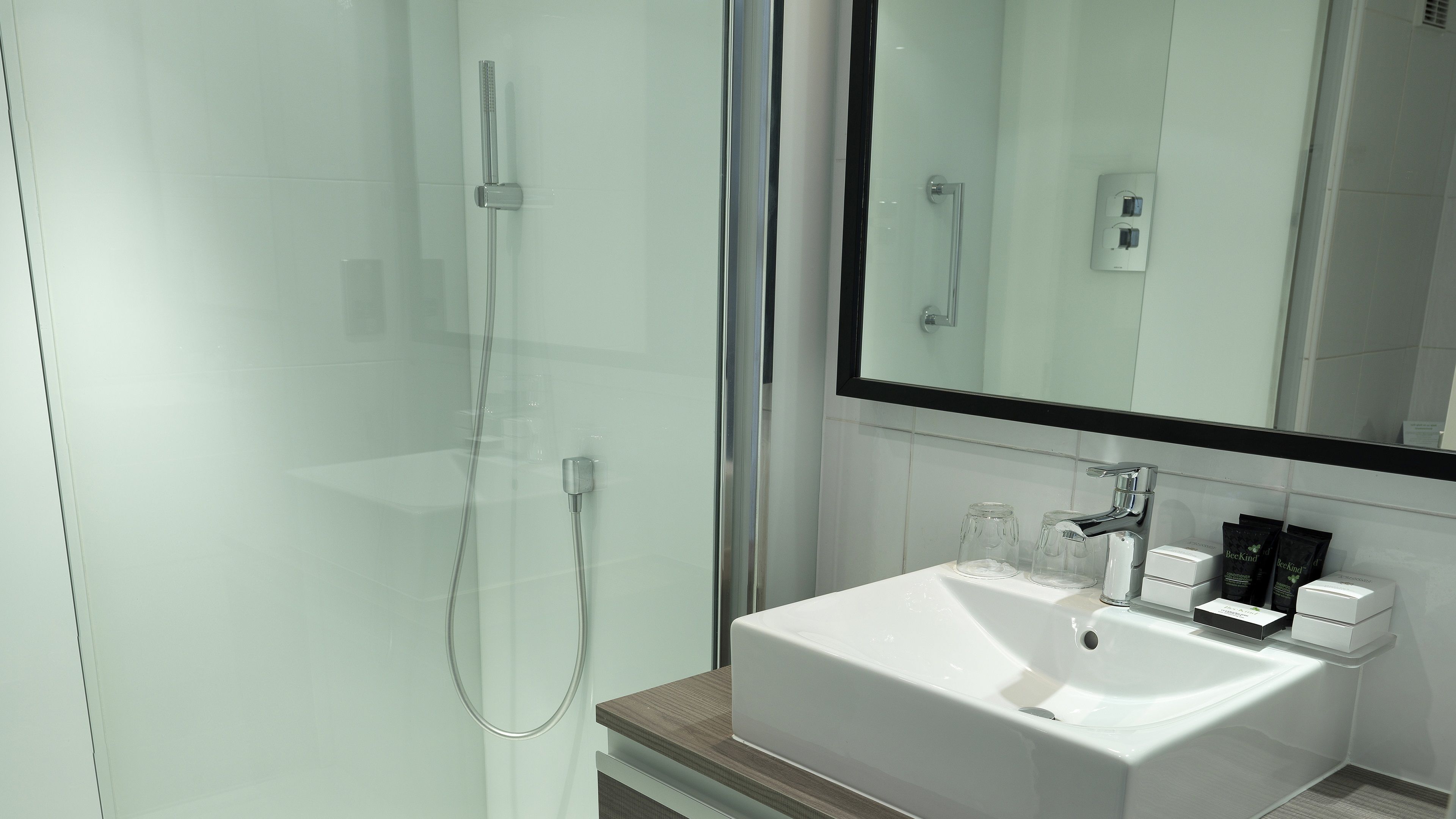 A modern bathroom with a glass-enclosed shower, a white sink, and a large mirror.