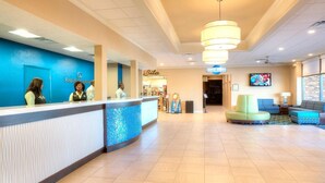 A hotel lobby with a reception desk, a TV mounted on the wall, and a seating area with sofas.