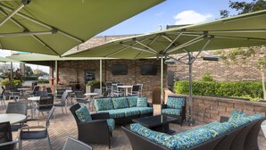 An outdoor patio with wicker furniture, green umbrellas, and brick walls.