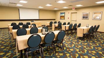 A conference room with multiple tables and chairs, a projector screen, and framed artwork on the walls.
