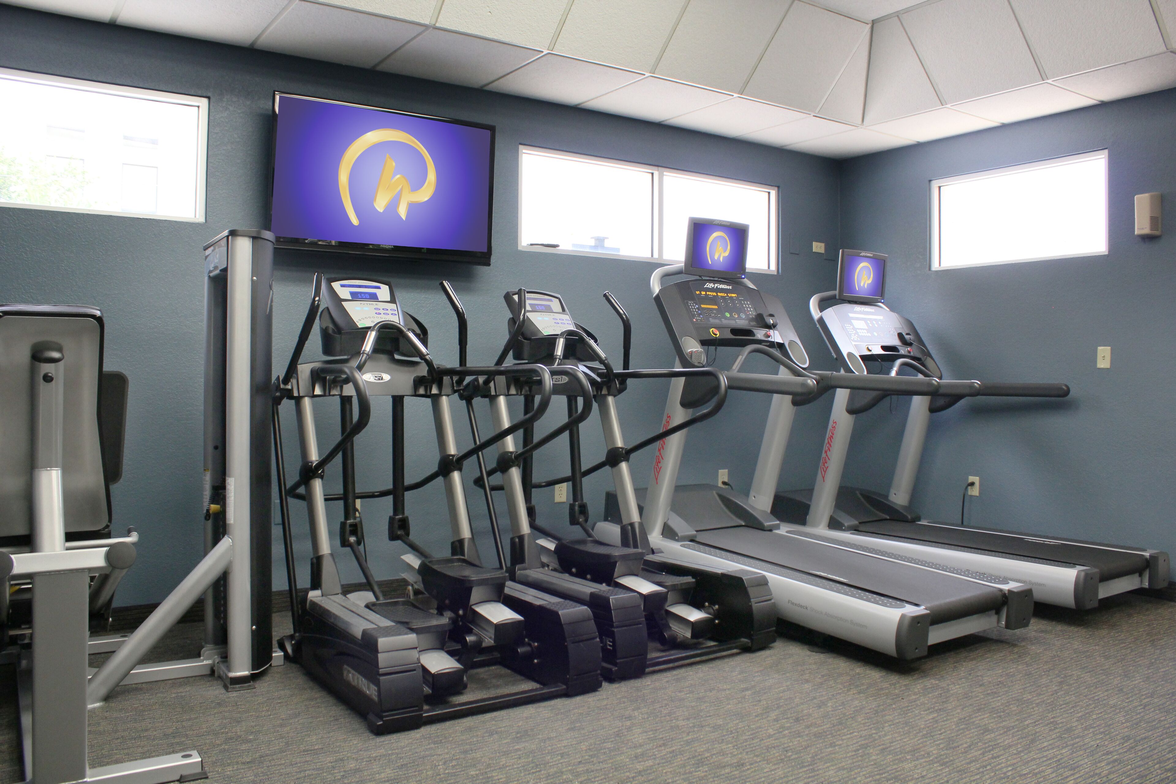 Un gimnasio con cintas de correr, elípticas y una bicicleta estática.