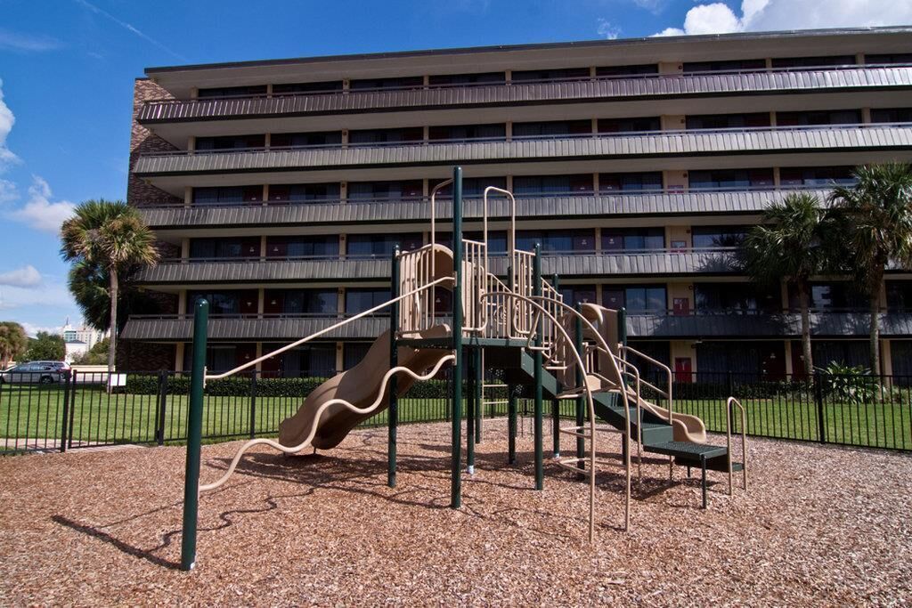 A playground with slides and climbing structures in front of a multi-story building with balconies.