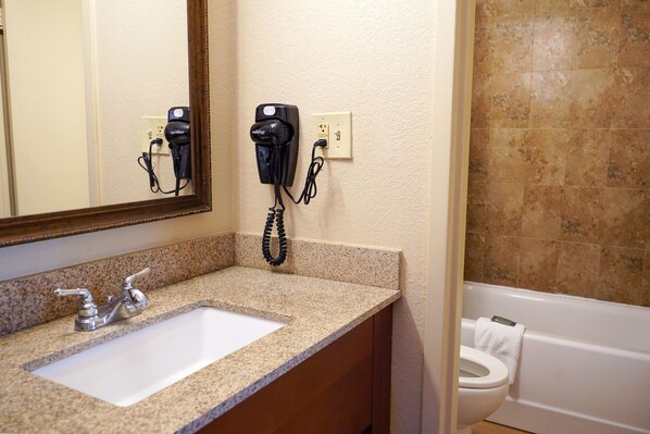 A bathroom with a granite countertop sink, a mirror, a hairdryer, and a toilet.