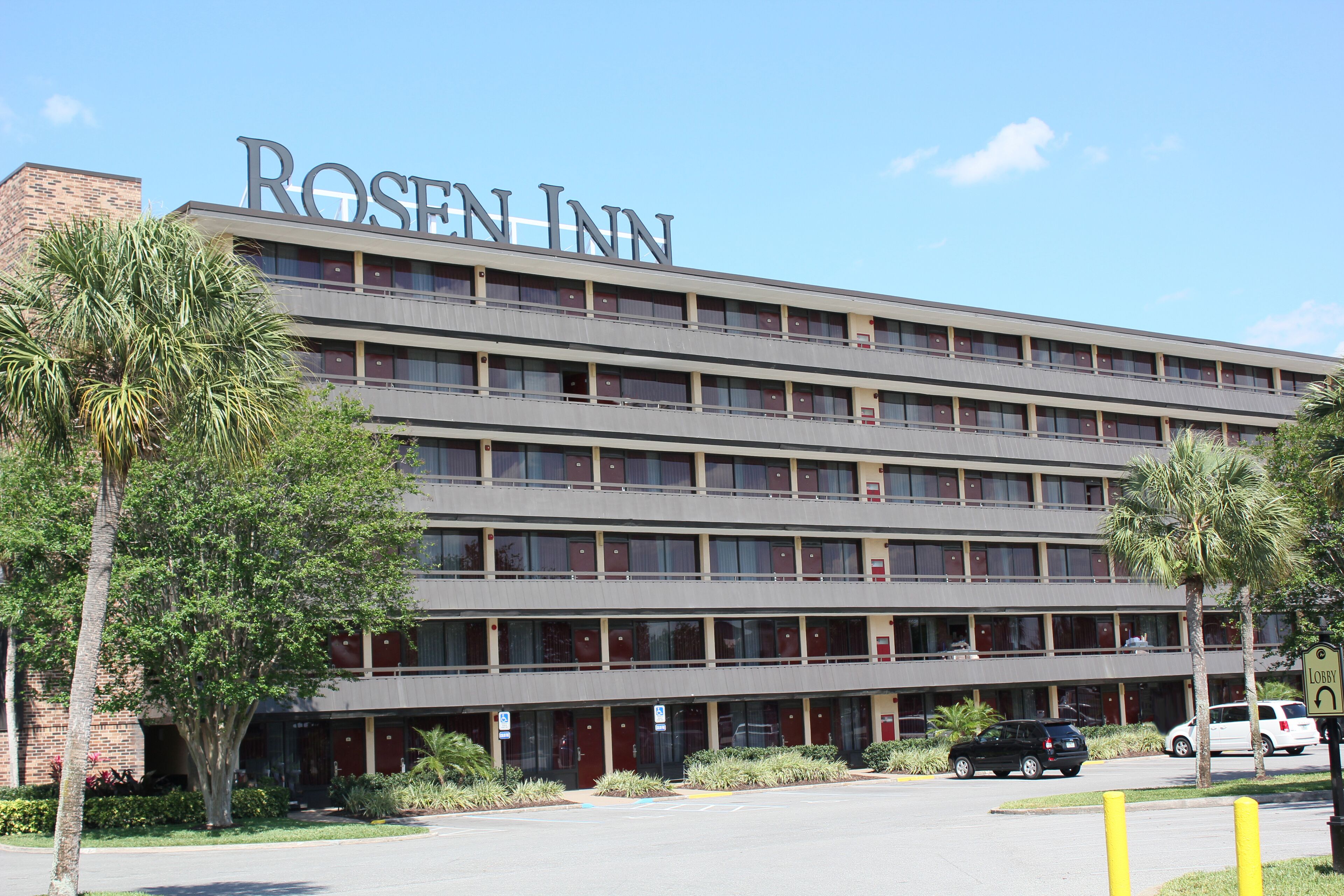 A multi-story Rosen Inn building with a flat roof, large windows, and a parking lot in front.