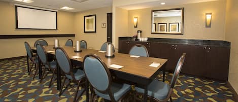 A conference room with a long table, chairs, a projector screen, and a coffee station.