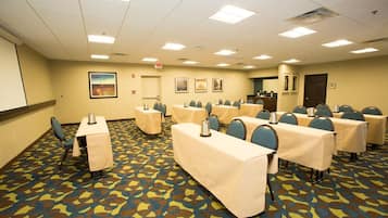 A conference room with tables and chairs, a projector screen, and a patterned carpet.