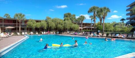 A swimming pool surrounded by lounge chairs and palm trees, with a building in the background.
