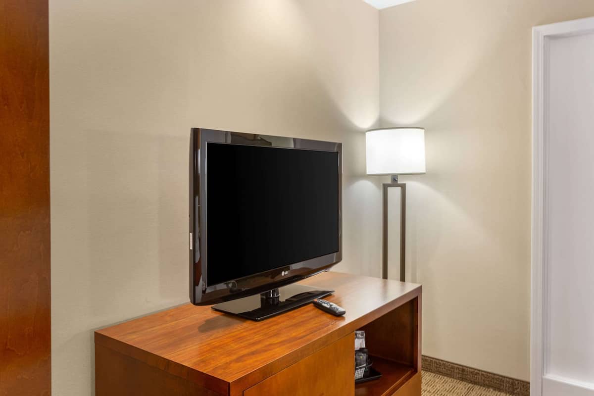 A flat-screen TV on a wooden stand in a hotel room, with a remote control on the stand and a lamp to the right.