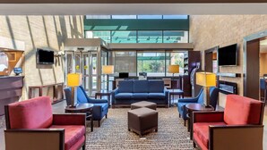 A hotel lobby with a blue sofa, red armchairs, a brown ottoman, and a TV mounted on the wall. - Comfort Suites Oakbrook Terrace - Chicago West (Villa Park)