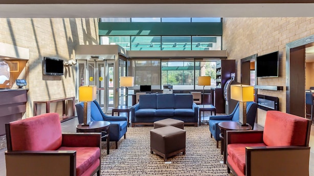 A hotel lobby with a blue sofa, red armchairs, a brown ottoman, and a TV mounted on the wall. - Comfort Suites Oakbrook Terrace - Chicago West (Villa Park)