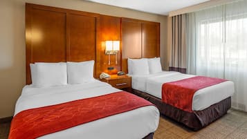 A hotel room with two beds, a nightstand with a phone and lamp, and a large window with curtains.