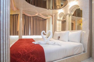 Habitación de hotel con una cama grande, un edredón rojo estampado y dos toallas con forma de cisne.