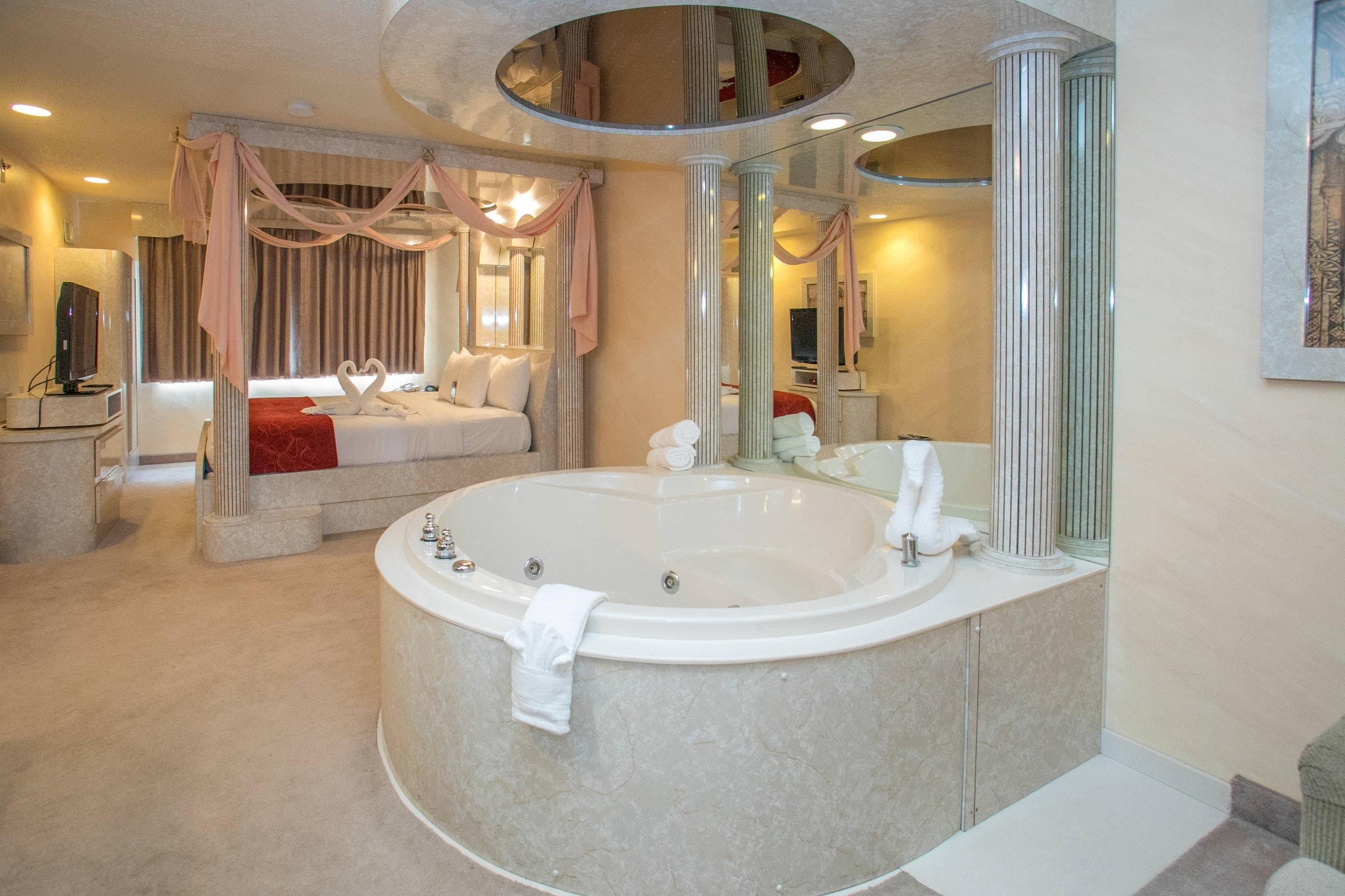 Ein luxuriöses Badezimmer mit einer großzügigen Badewanne, ein separater Schlafbereich mit einem Bett und einem Spiegel mit runder Rahmung.