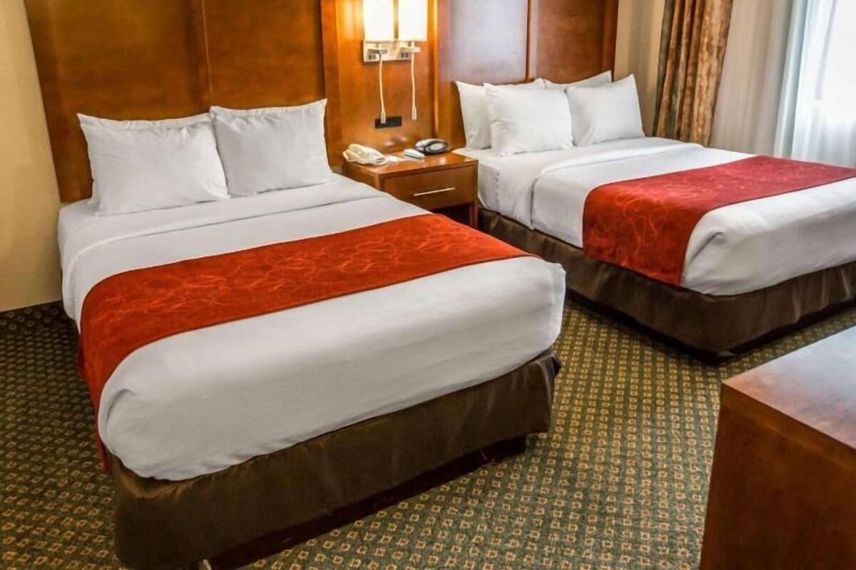 A hotel room with two beds, a nightstand, a lamp, and a window with curtains.