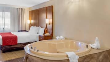 Habitación de hotel con una cama grande, una mesita de noche con lámpara, un baño con bañera y zona de ducha.