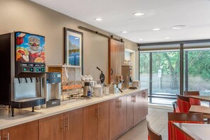 A modern kitchen area with a juice dispenser, a coffee machine, and a view of the outdoors. - Comfort Suites Oakbrook Terrace - Chicago West (Villa Park)