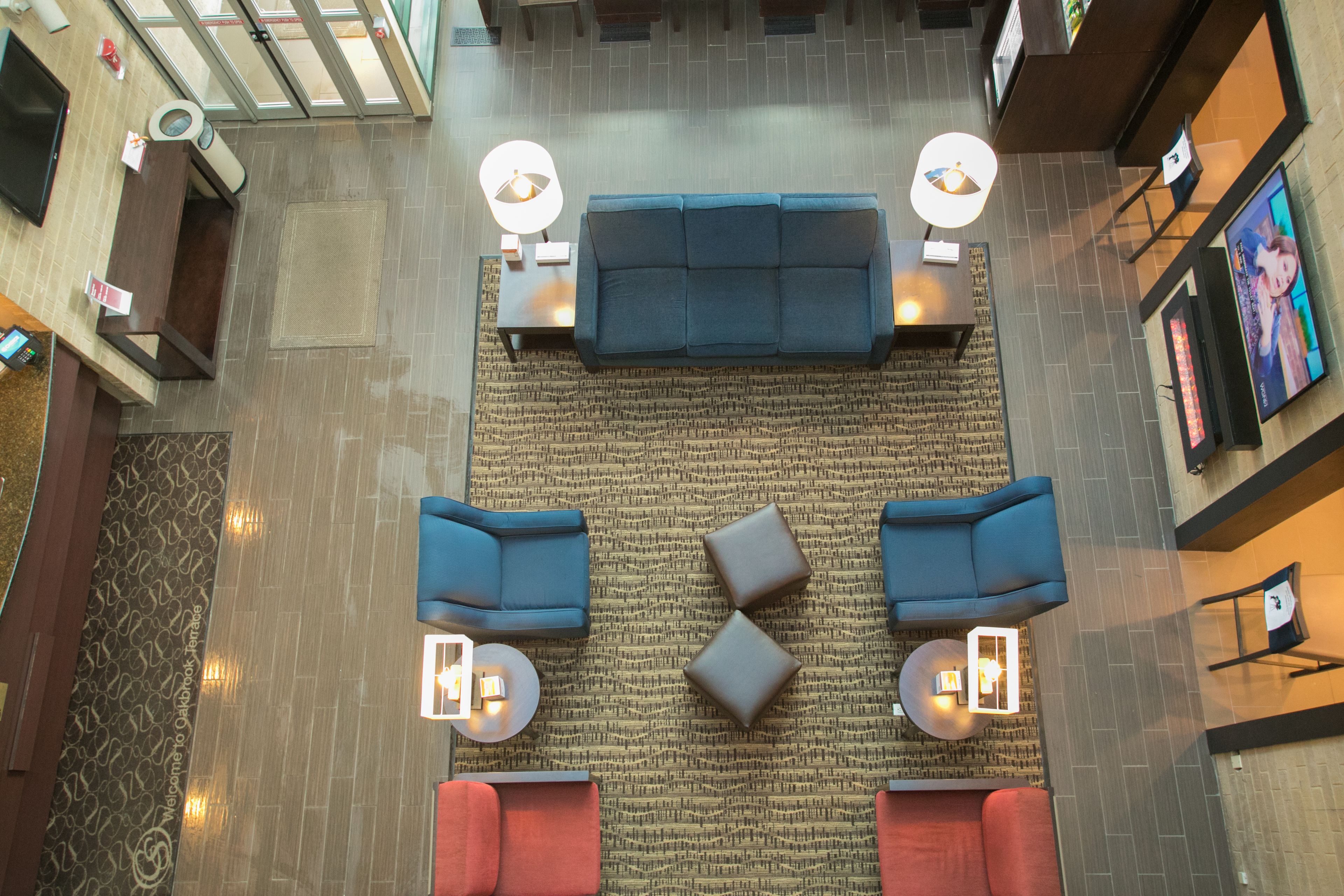 A spacious lobby with a central blue sofa, two armchairs, and a coffee table, surrounded by a patterned rug.