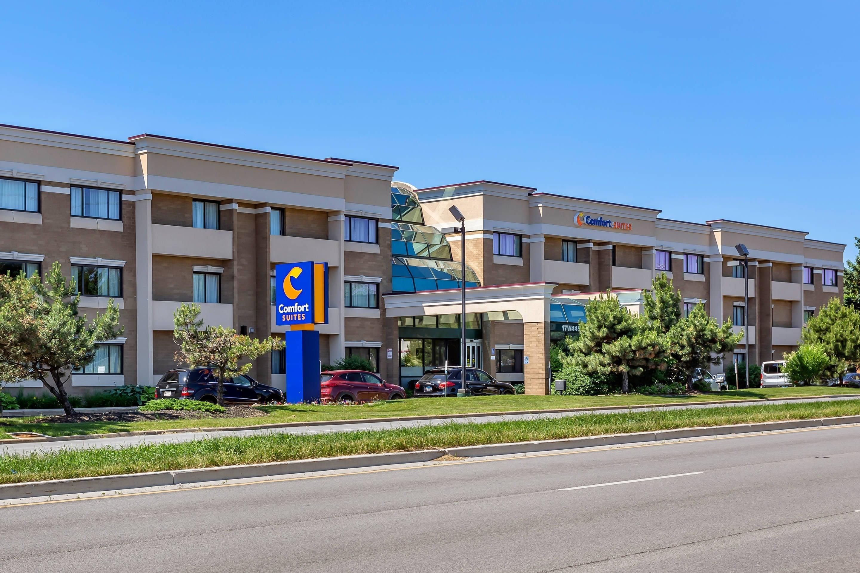 A hotel with a modern design, featuring a prominent Comfort Suites sign, multiple parking spaces, and a well-maintained lawn.