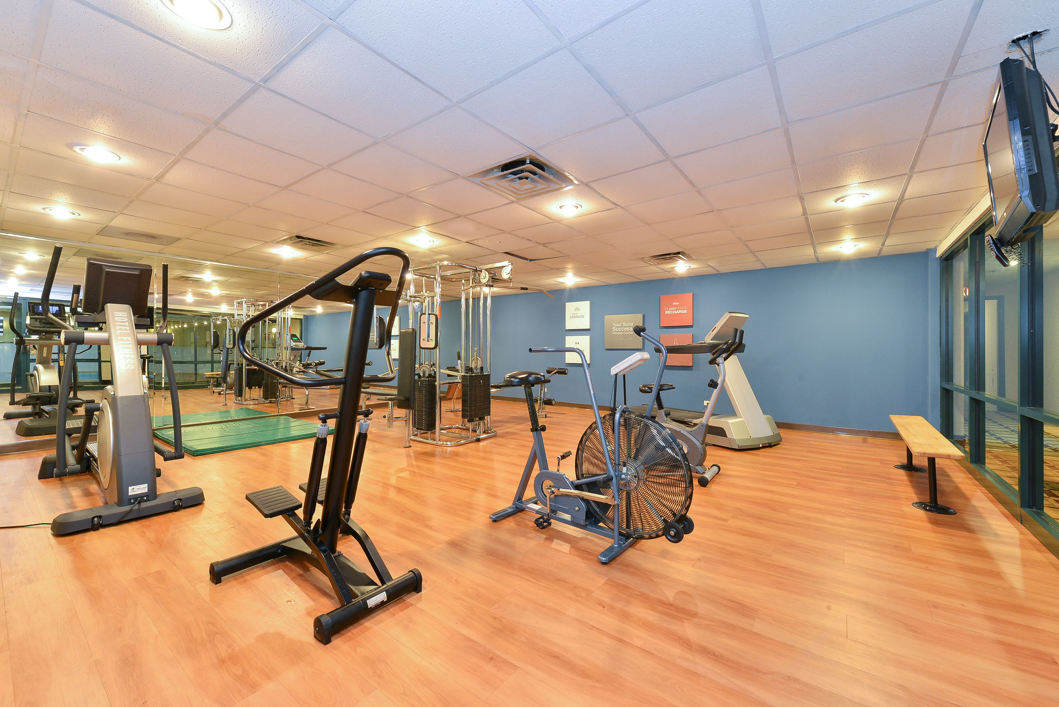 A gym with various exercise equipment, a green mat area, and a wooden floor.