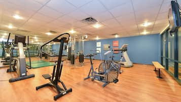 A gym with various exercise equipment, a green mat area, and a wooden floor.