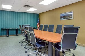 Une salle de conférence avec une longue table, des chaises, un drapeau et un tableau représentant un paysage urbain.