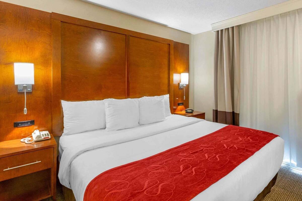 A hotel room with a large bed, wooden headboard, bedside lamps, a telephone, and a window with curtains.