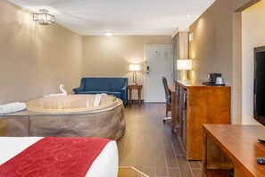 A hotel room with a large bed, a sitting area with a sofa and armchairs, a desk with a chair, a television, and a bathroom with a bathtub. - Comfort Suites Oakbrook Terrace - Chicago West (Villa Park)
