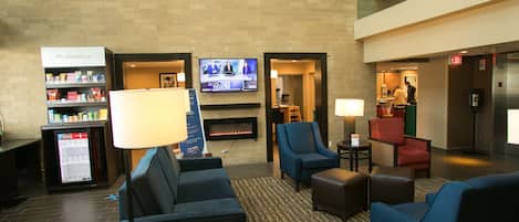 A hotel lobby with seating areas, a television, a fireplace, and a vending machine.
