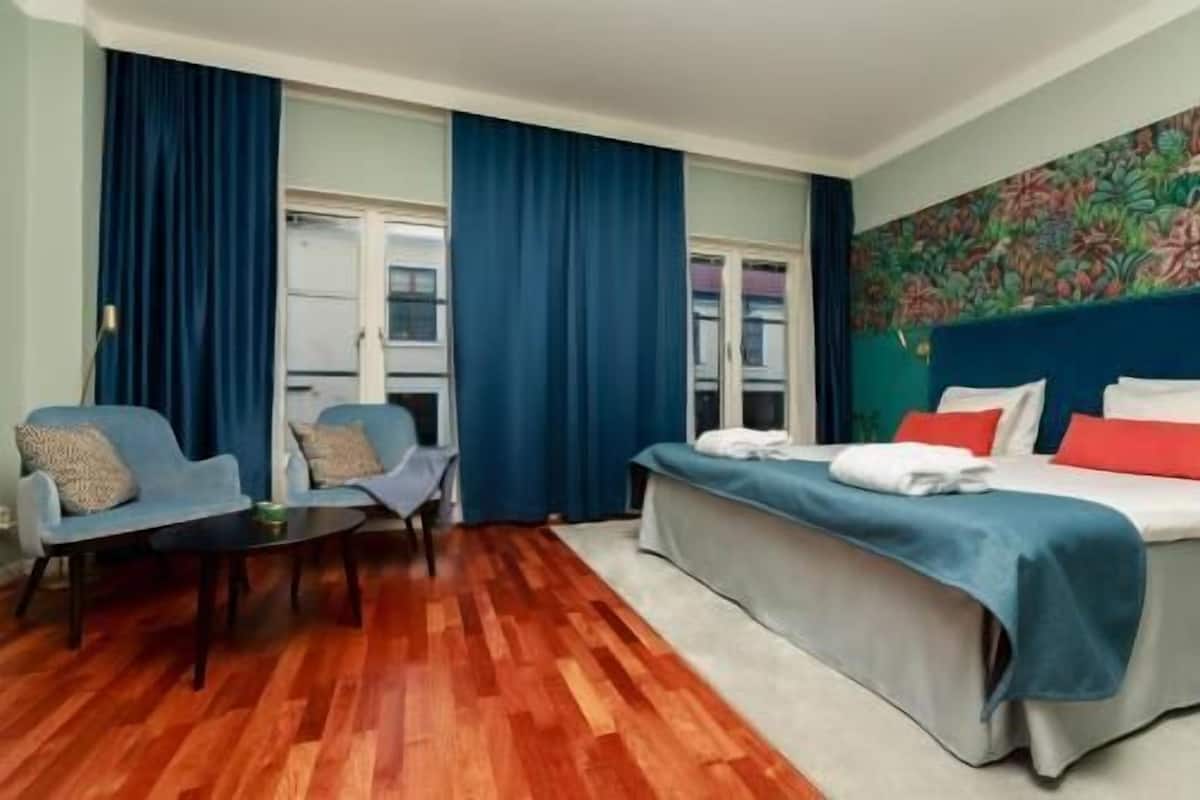 A hotel room with a bed, two chairs, a small table, and a window with curtains.