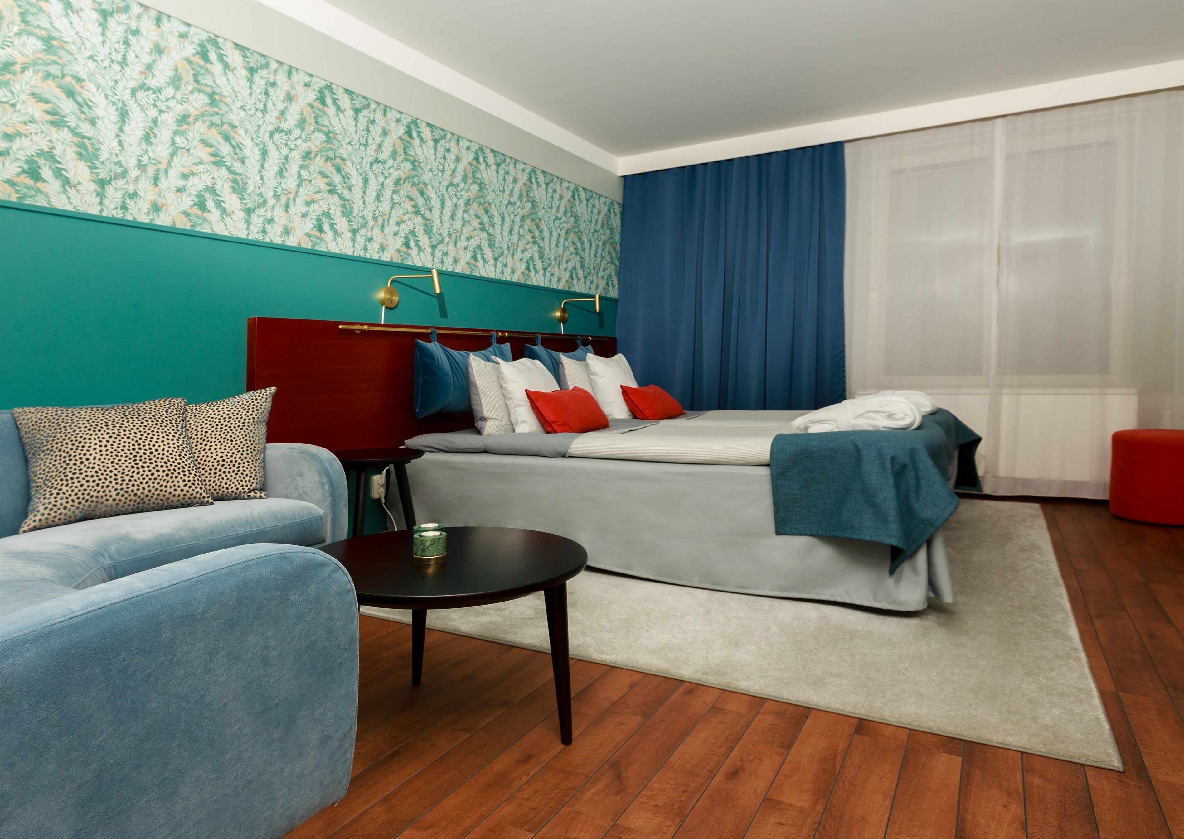 A modern hotel room with a bed, a sofa, a small table, and a red ottoman.