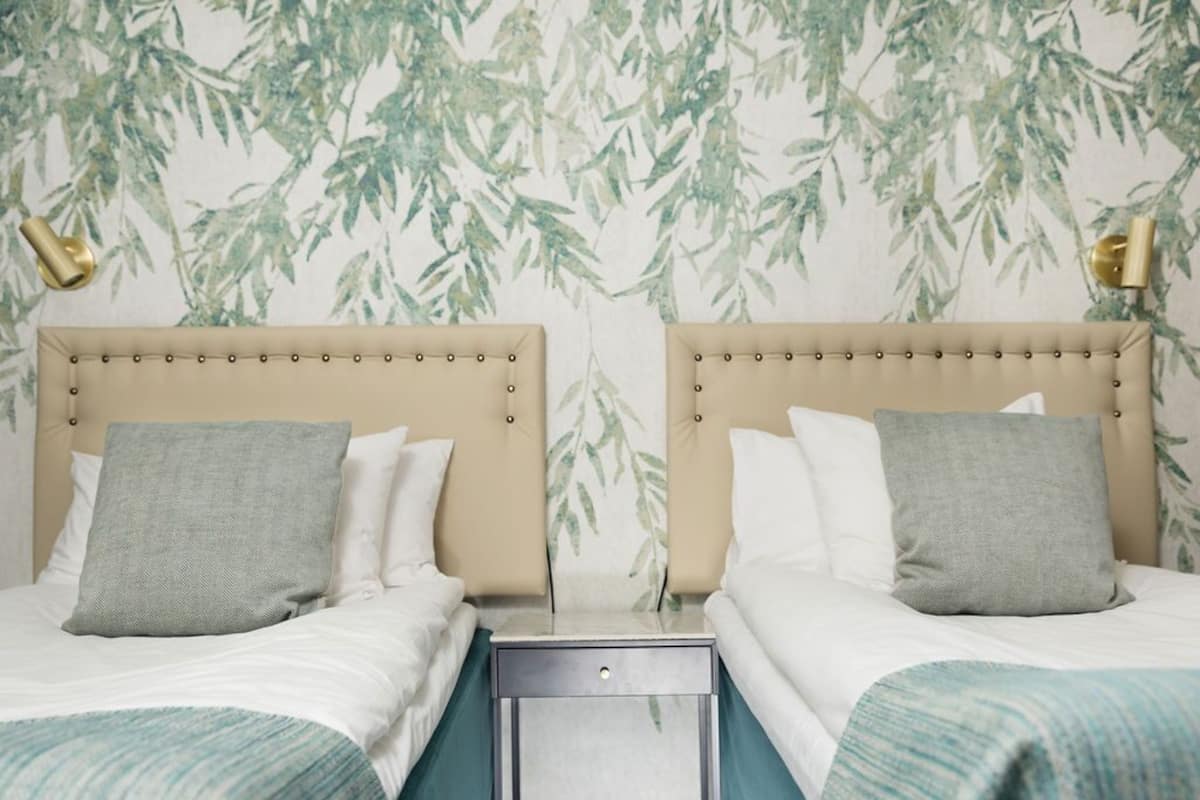 A hotel room with two beds, a nightstand, and a wall with a bamboo leaf pattern.