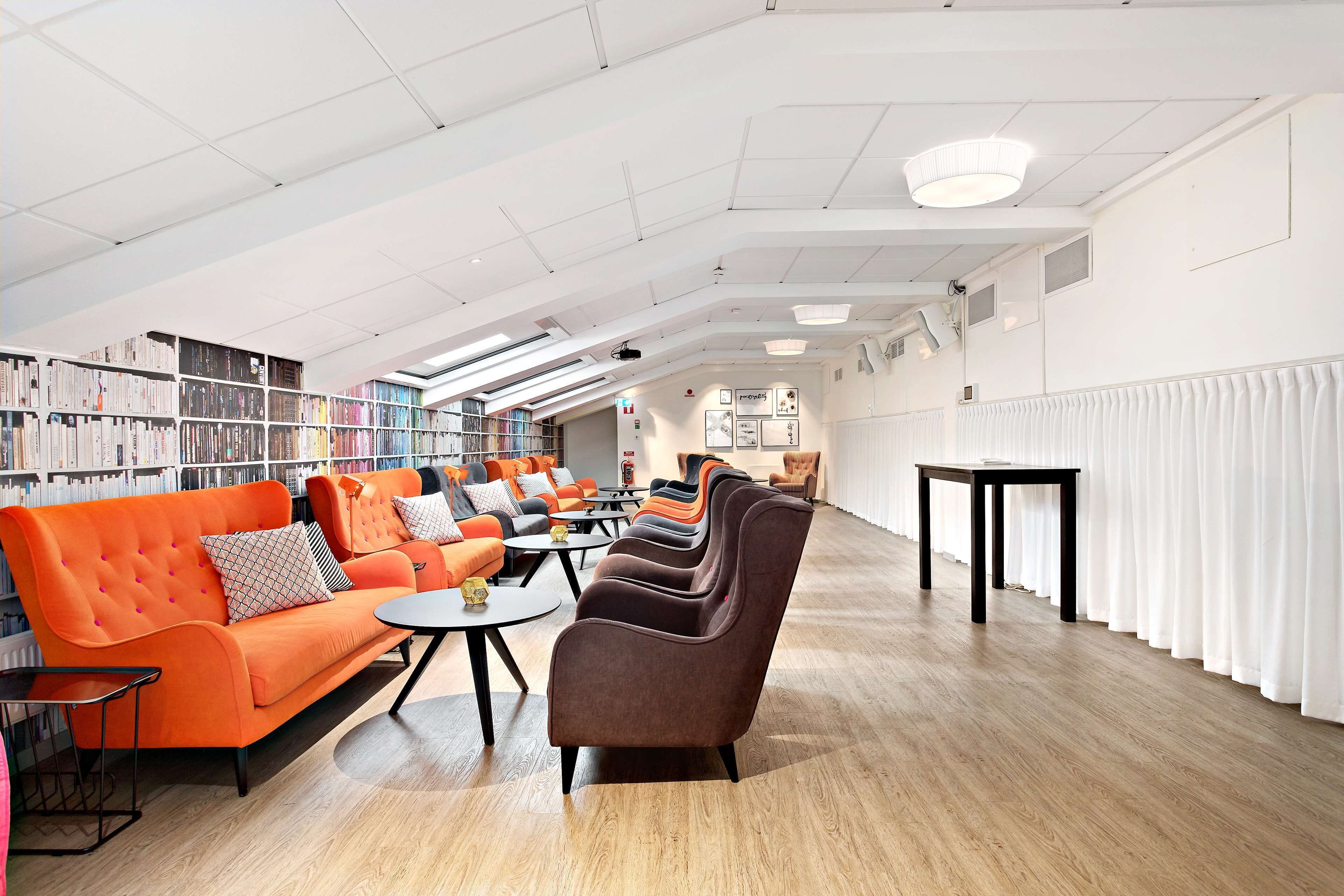 Une bibliothèque dotée d’étagères, d’un plafond lumineux et d’un espace détente avec des canapés et des tables.