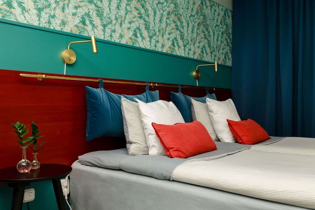 A bed with a red headboard, multiple pillows, and a bedside table with a plant.