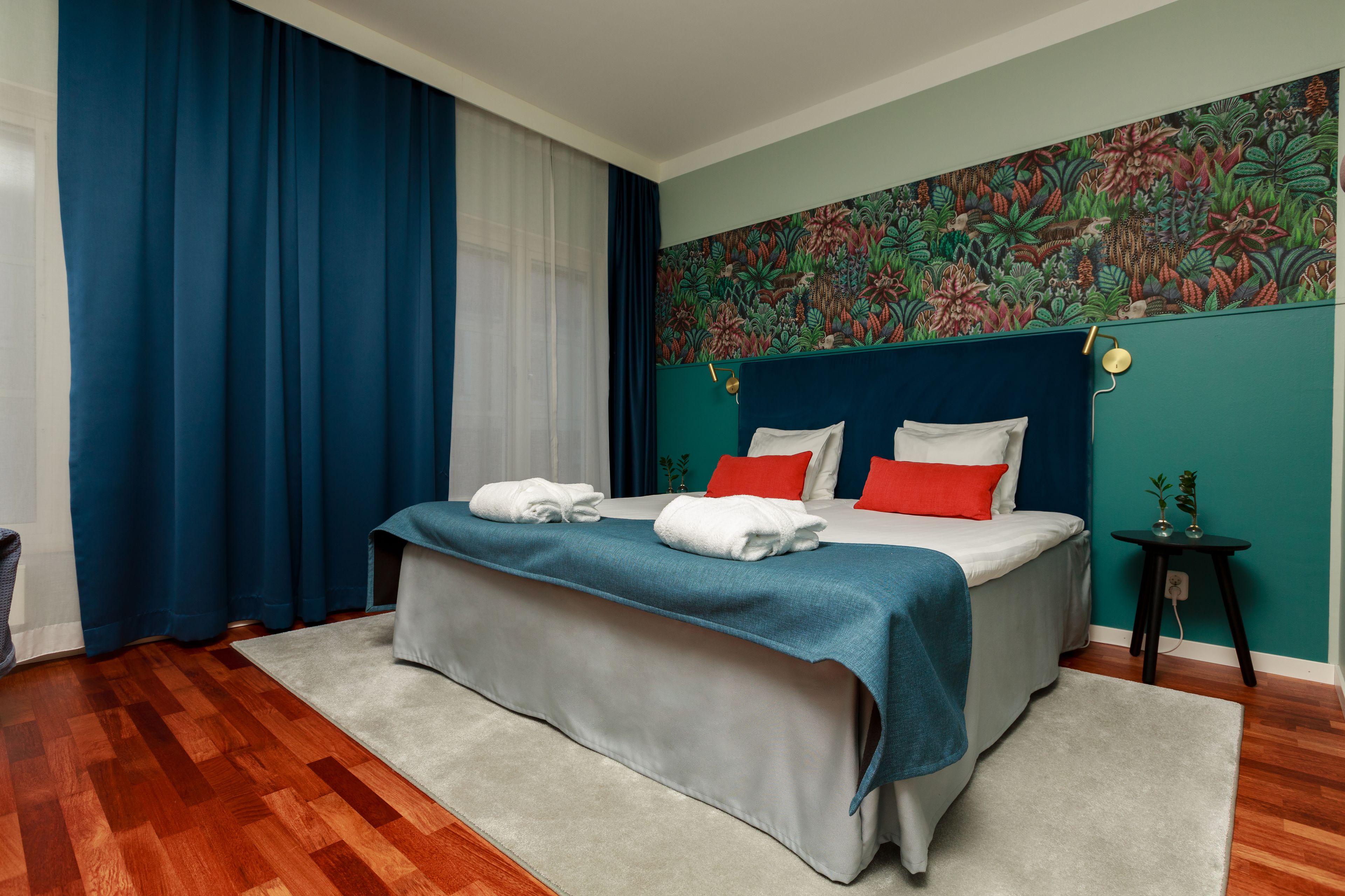 Una habitación de hotel con cama, cabecera azul, papel tapiz floral y piso de madera.