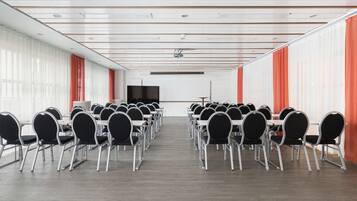 Un salón de conferencias con filas de mesas y sillas, un proyector y una pantalla grande.