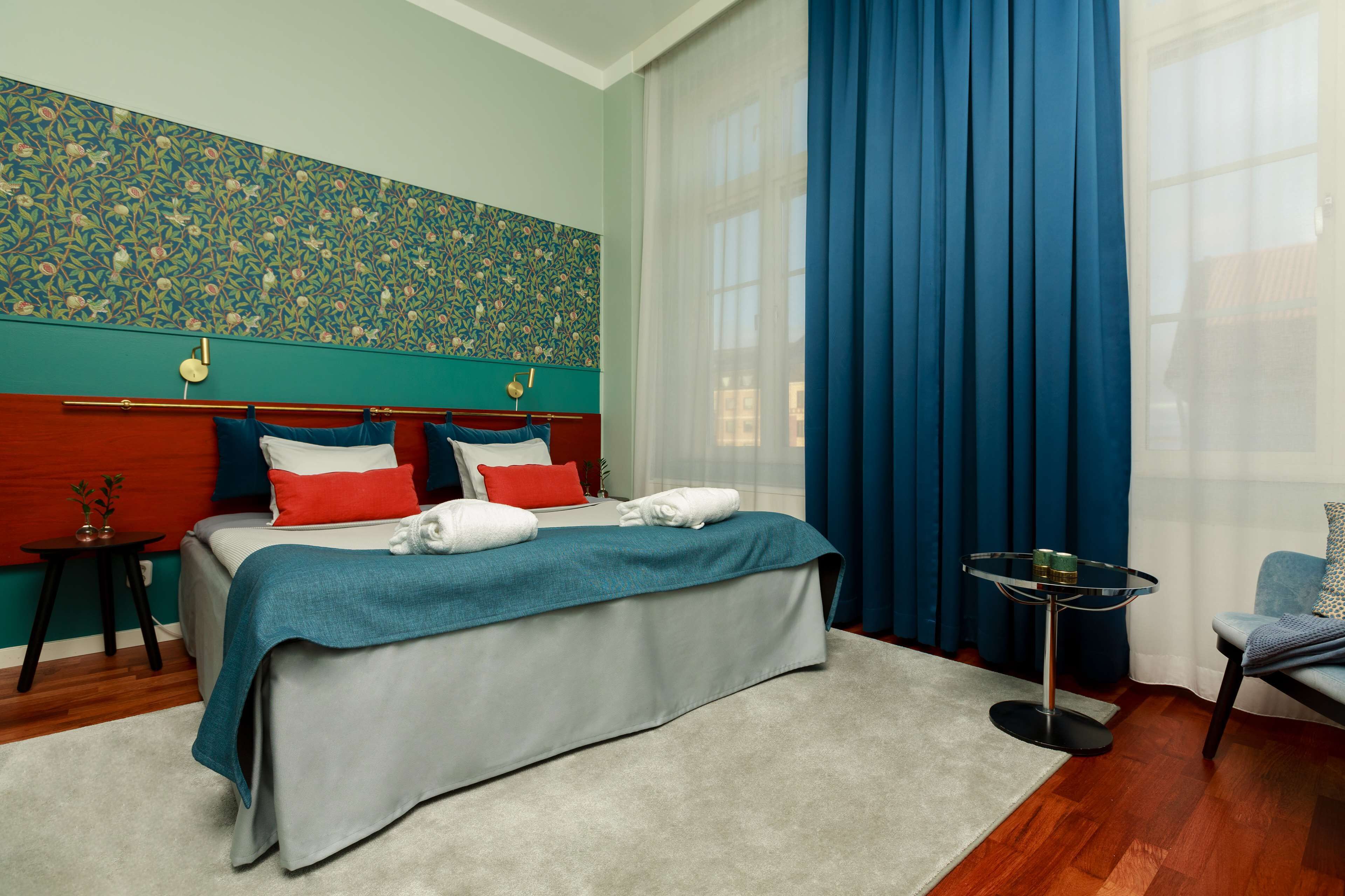 Un dormitorio con cama, mesita de noche, silla y ventana con cortinas.
