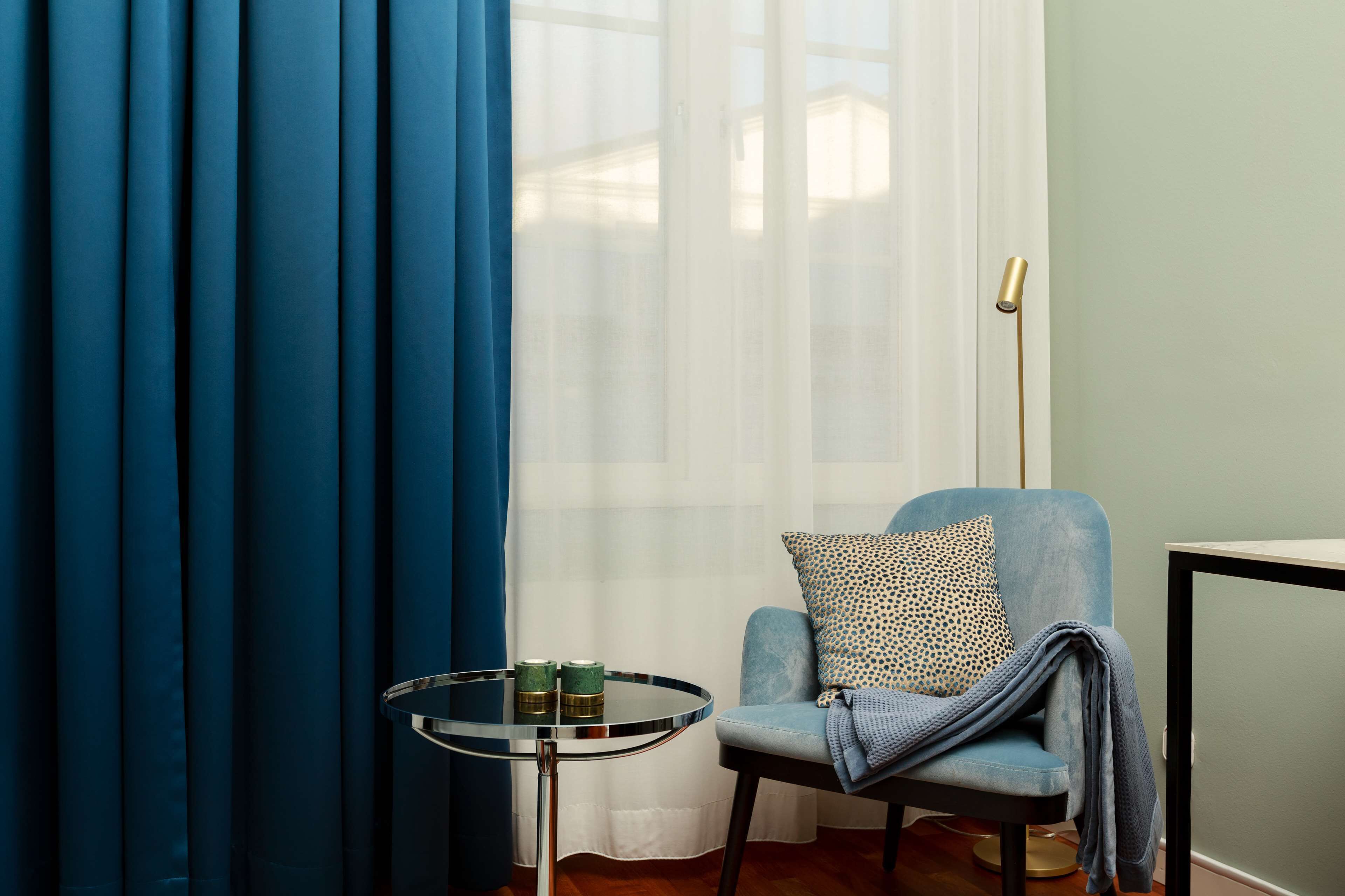 A room with a blue chair, a small round table with two green candles, and a floor lamp.