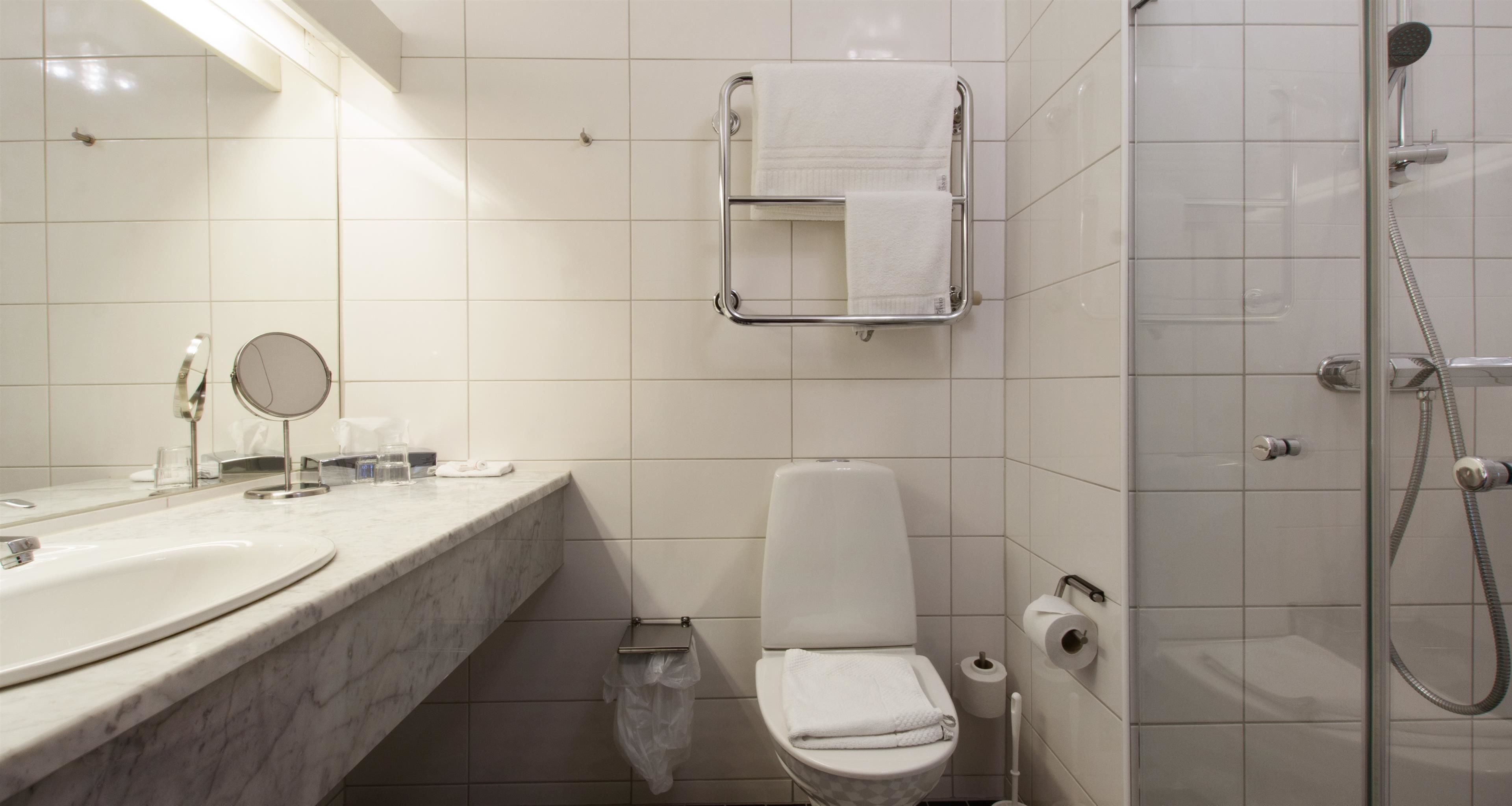 Un baño moderno con lavamanos de mármol, inodoro, ducha y toallero.